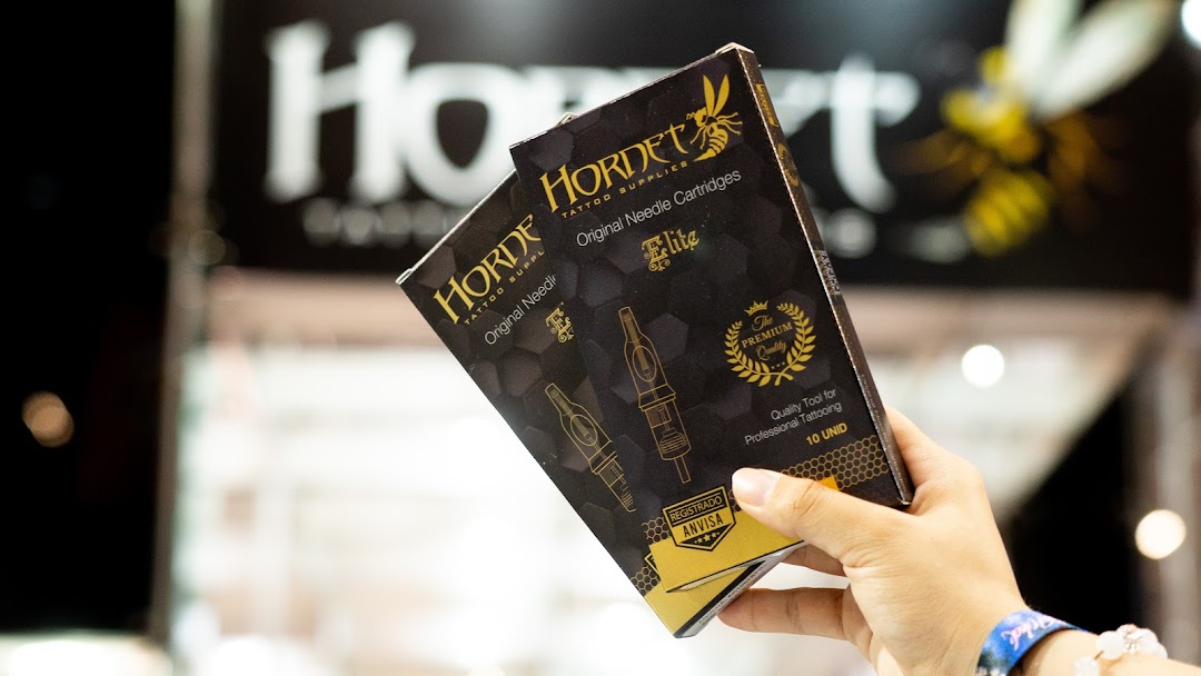 A hand holds boxes of Hornet Tattoo Supplies Original Needle Cartridges.