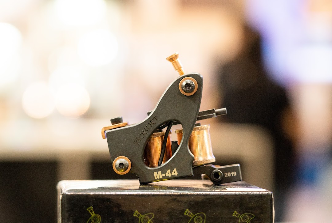 A close-up of a black tattoo machine with copper coils, labeled 'HORNET M-44'.
