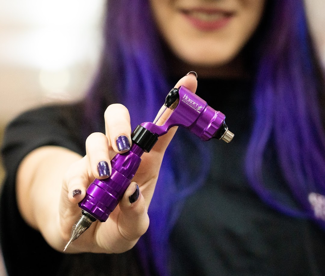 A person with purple hair holds a purple tattoo machine.