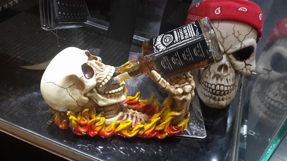A skull figurine holding a bottle of Jack Daniel's whiskey, with flames at its base.