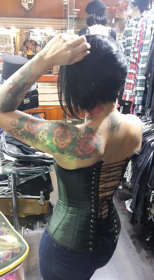 A person wearing a corset and jeans, with tattoos, in a clothing store.