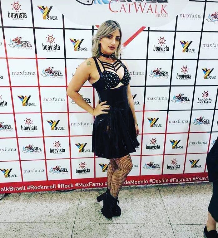 A woman in a black rock-inspired outfit poses in front of a branded backdrop.