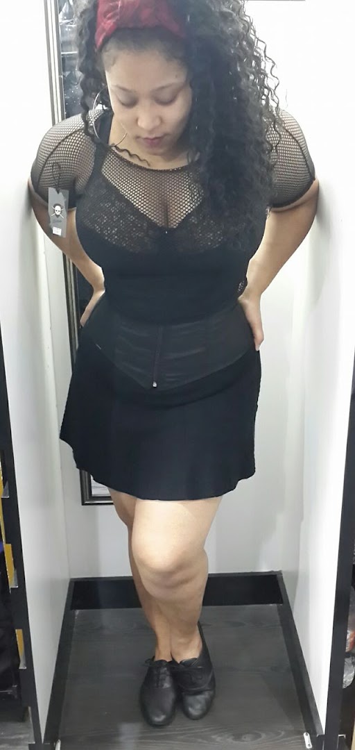 A woman models a black fishnet top and skirt with black shoes.