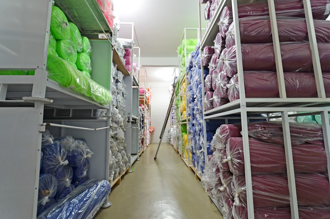 A warehouse aisle filled with shelves stacked high with rolls of colorful fabric.