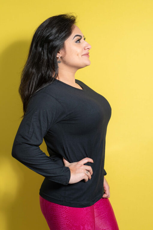 A woman with dark hair and dimples poses in a black long-sleeved shirt and pink patterned pants.