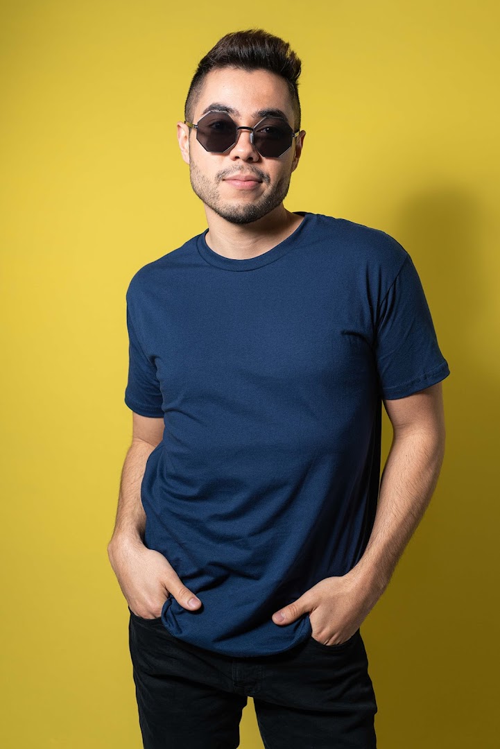 A man wearing a navy blue t-shirt and sunglasses poses against a yellow background.