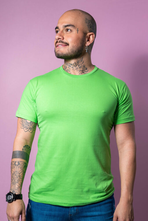 A man with tattoos and piercings wears a bright green t-shirt and blue jeans.