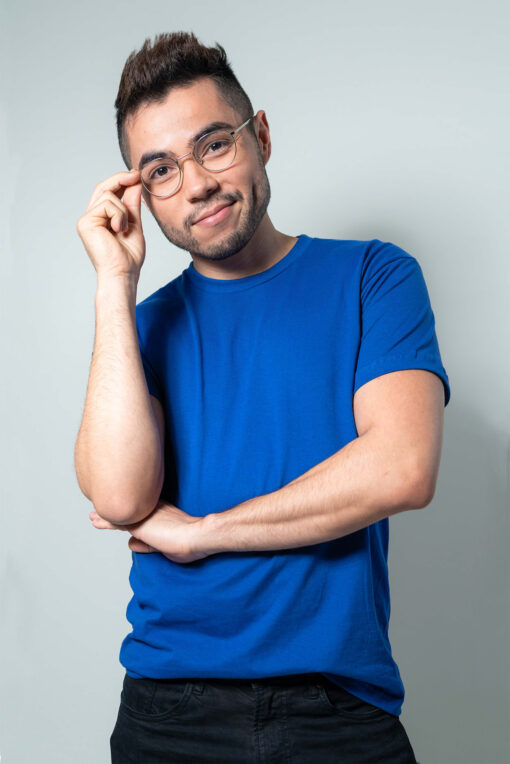 A man with glasses and a blue t-shirt poses against a light gray background.
