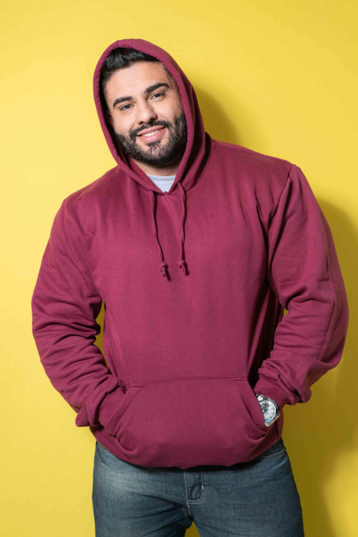 A man wearing a maroon hoodie and jeans poses against a bright yellow background.