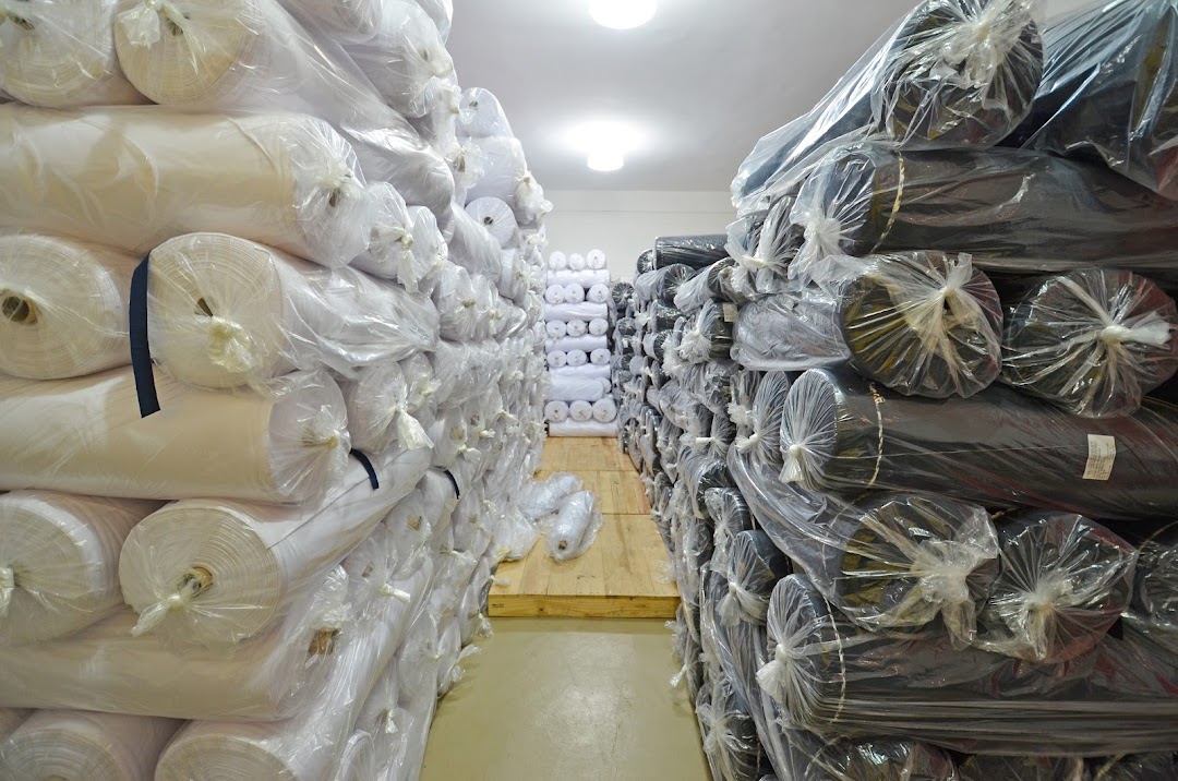 A warehouse aisle filled with stacks of fabric rolls, predominantly white and dark colors.