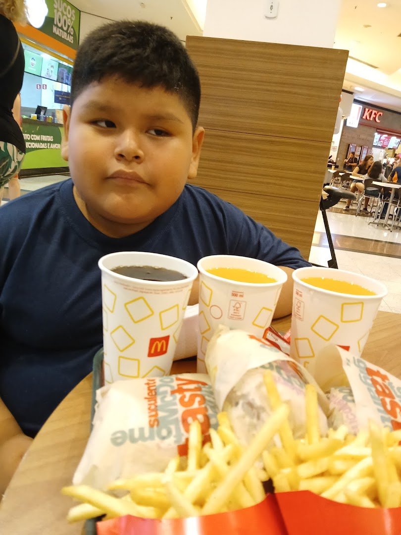A young boy sits at a table with McDonald's food and drinks, with KFC visible in the background.
