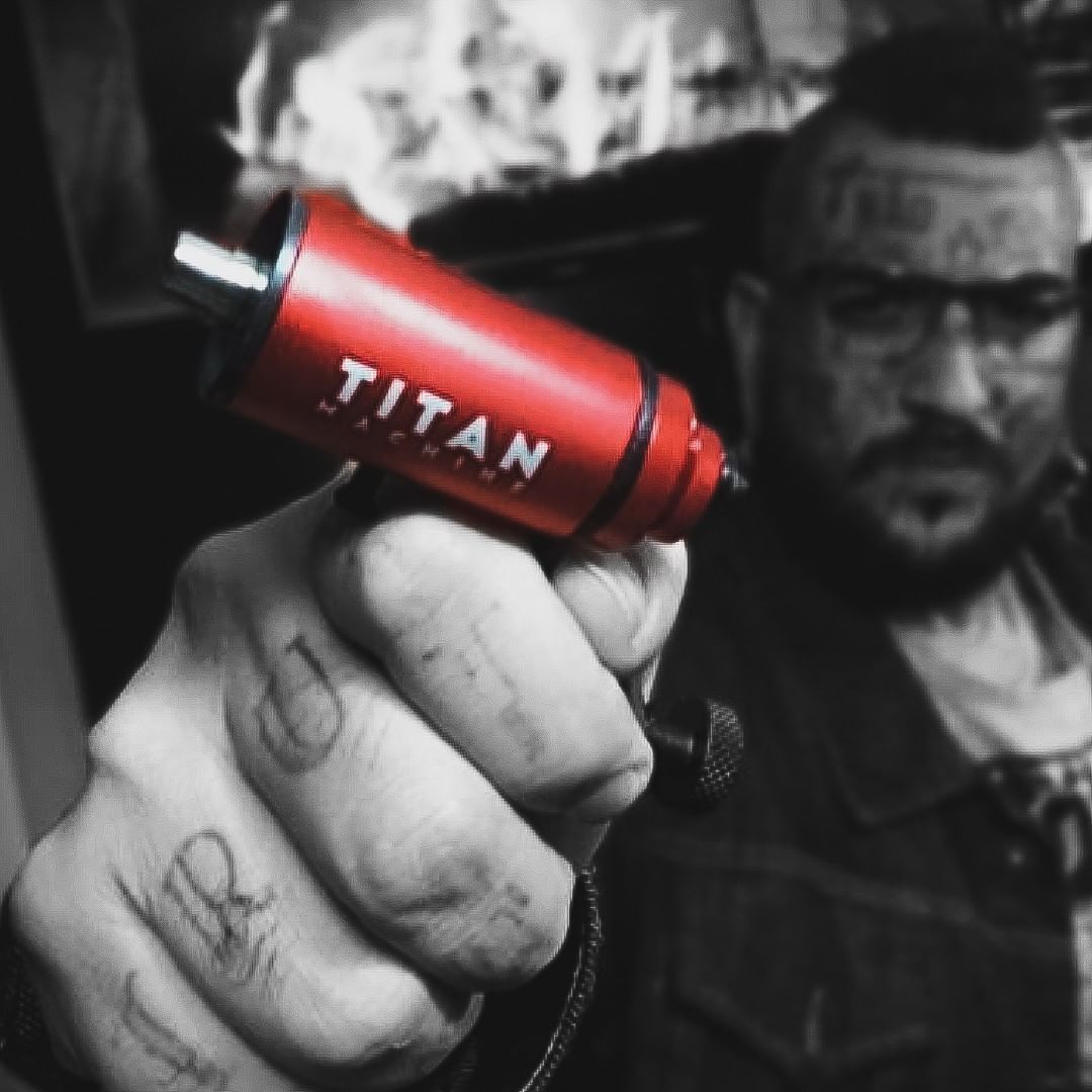 A person holds a red tattoo machine with the brand name 'TITAN' visible.