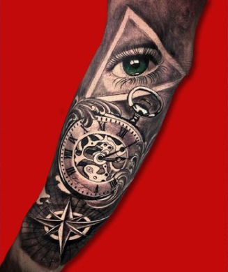A detailed tattoo on an arm featuring an eye, a pocket watch, and a compass rose.