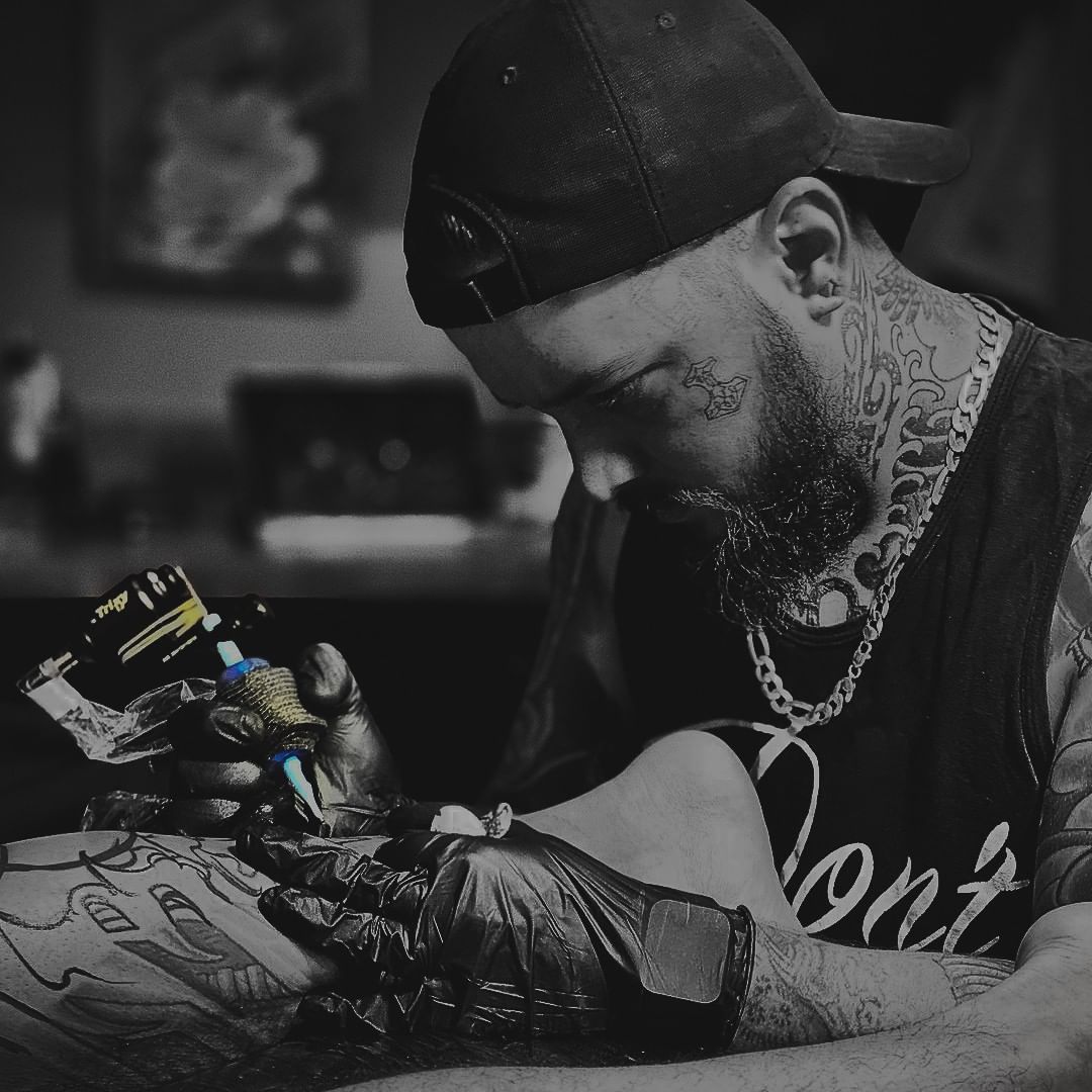 A tattoo artist in black gloves meticulously works on a client's leg with a tattoo machine.