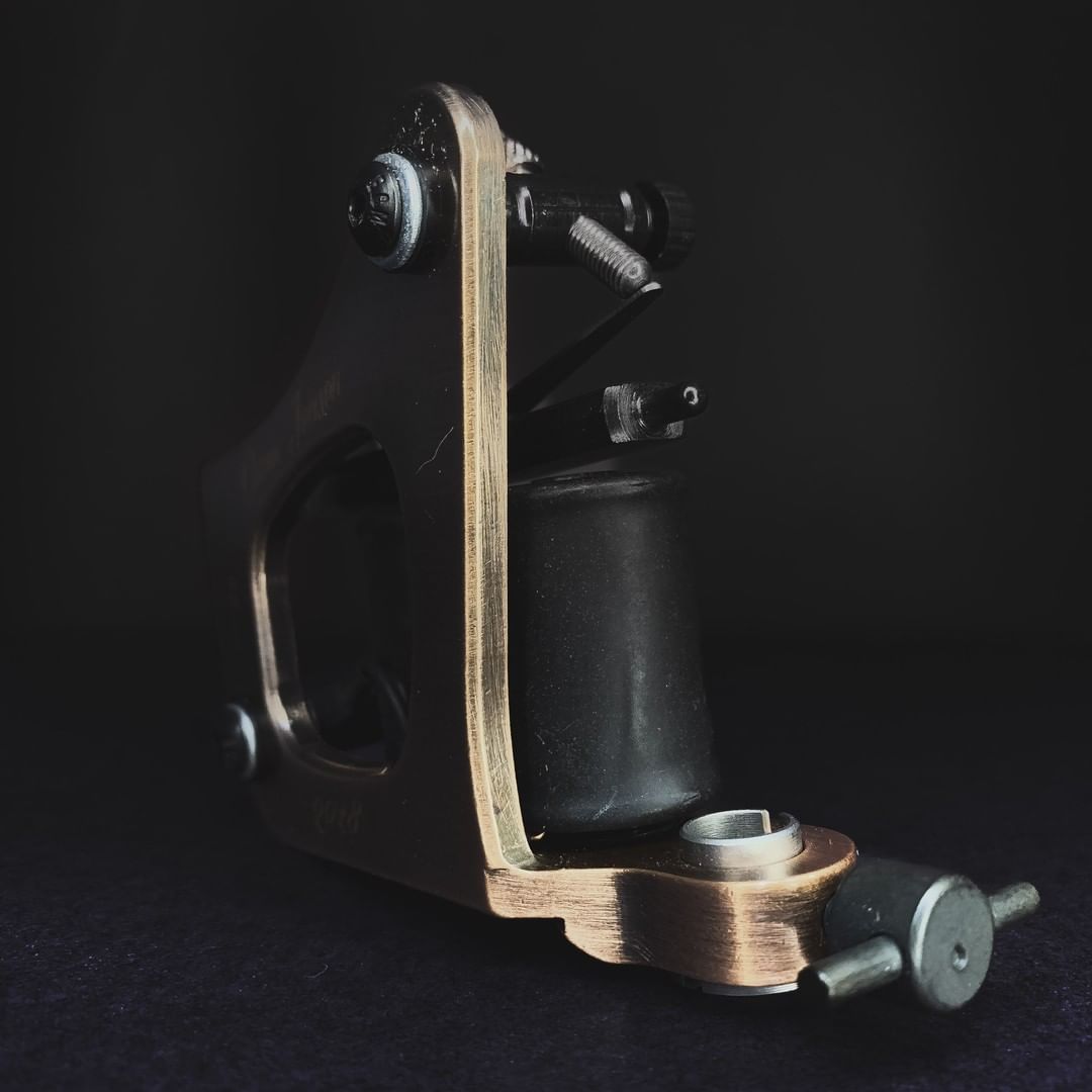 A close-up shot of a professional tattoo machine with a brass and black finish.