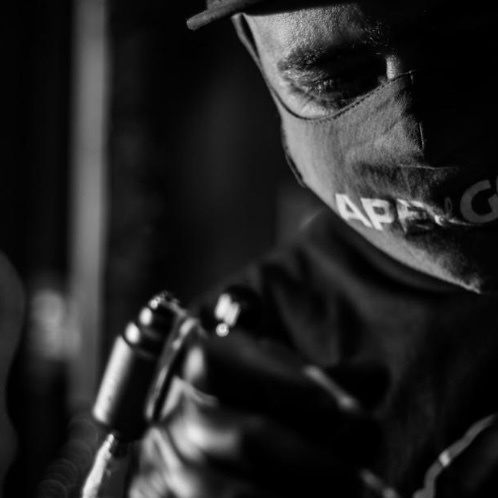 Close-up of a person wearing a mask and holding a tattoo machine.