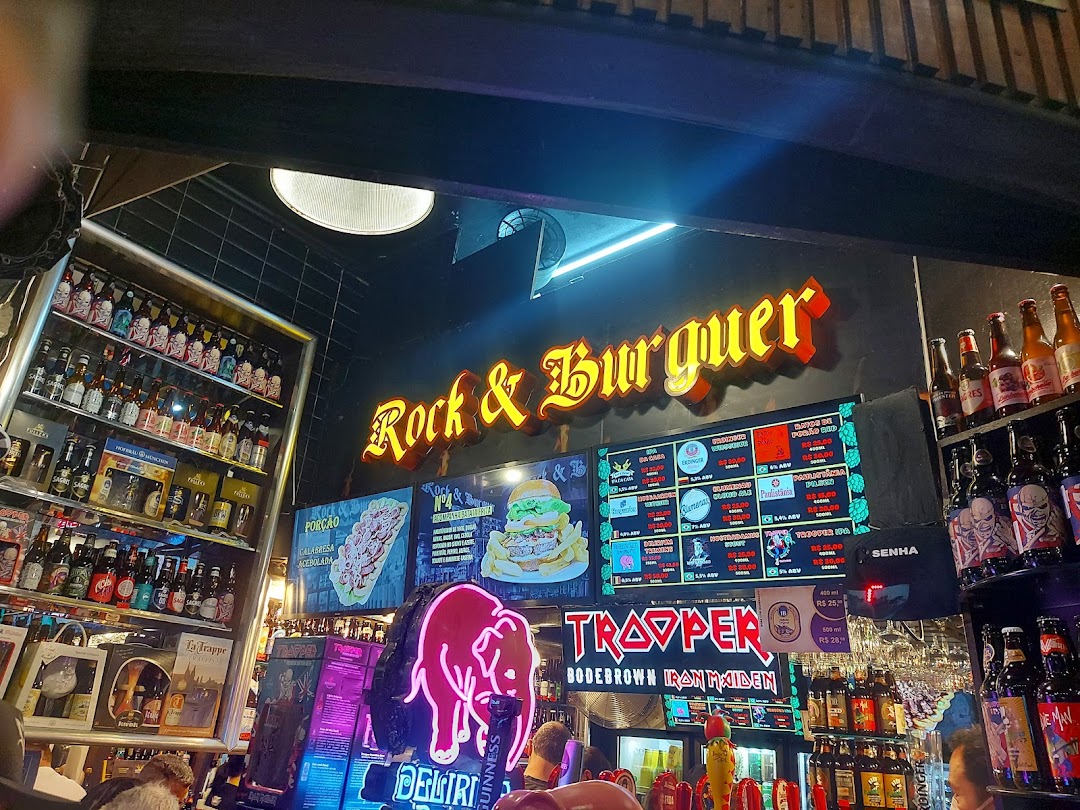 Interior of a rock-themed bar with neon signs, shelves of beer bottles, and a digital menu.