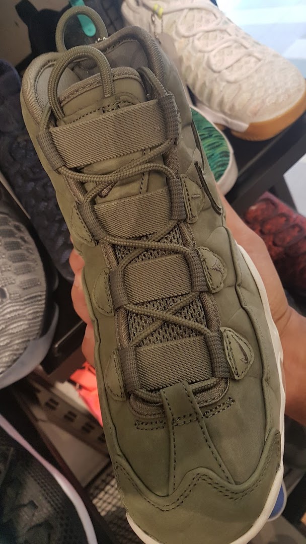 A close-up view of a person holding a green sneaker with intricate lacing.