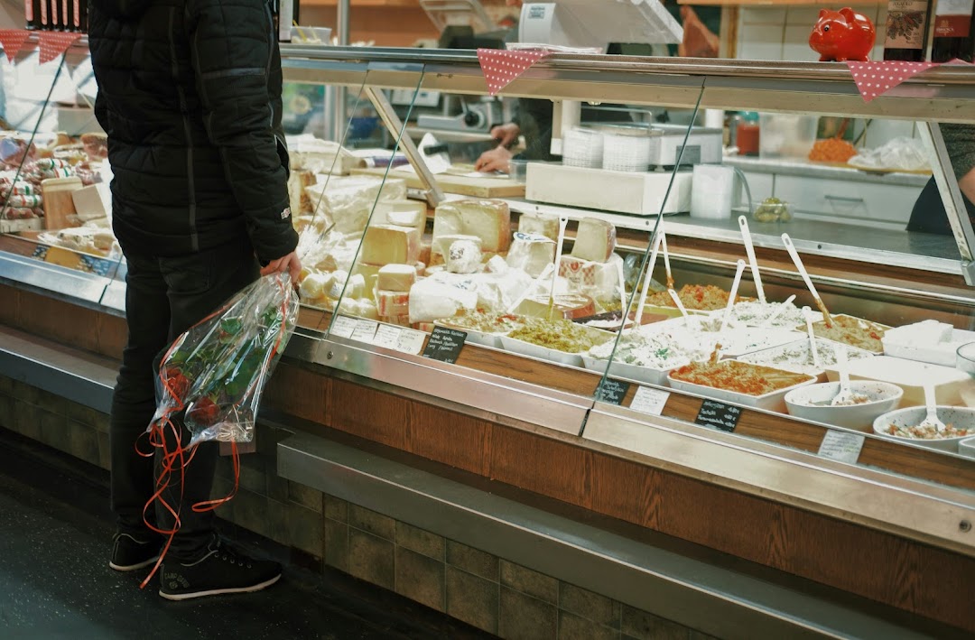 A person holding a bouquet of roses stands in front of a display case filled with various cheeses and prepared foods.