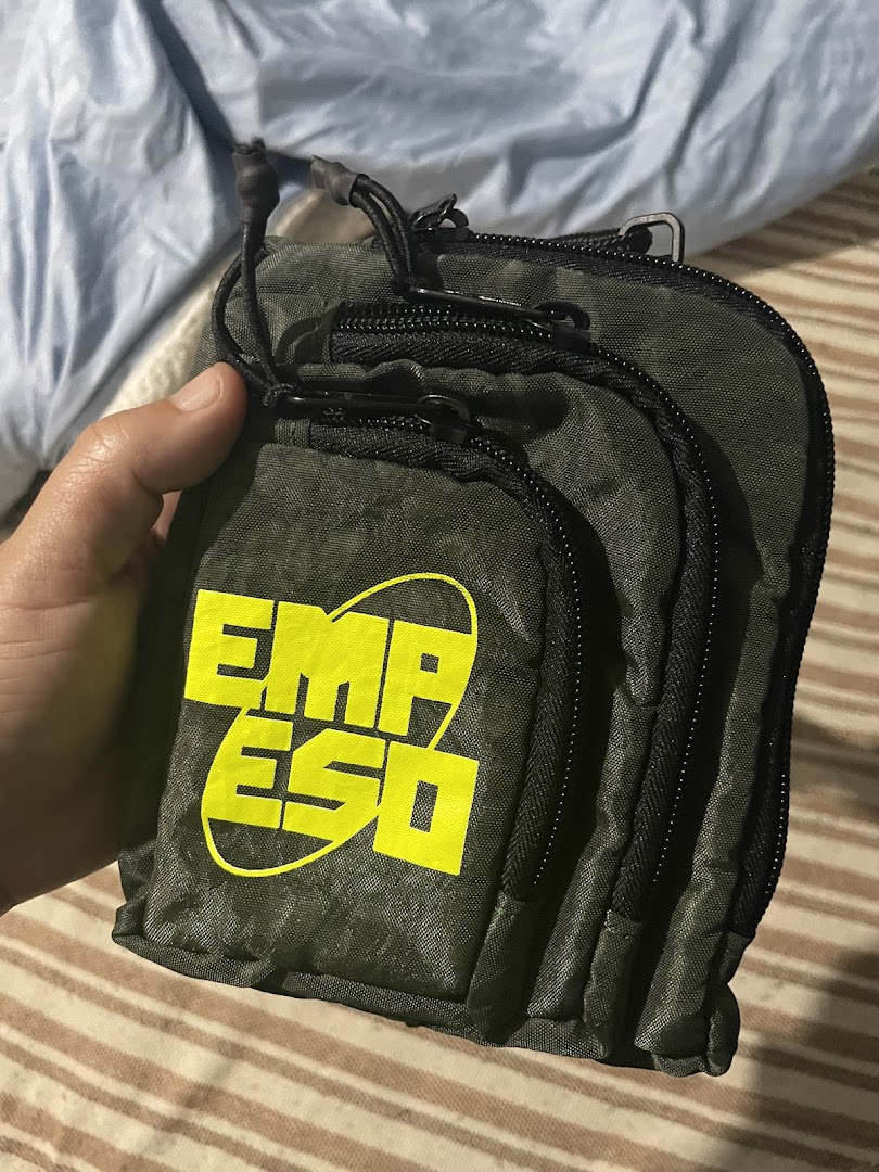 A hand holds a stack of dark green zippered pouches with a bright yellow logo.