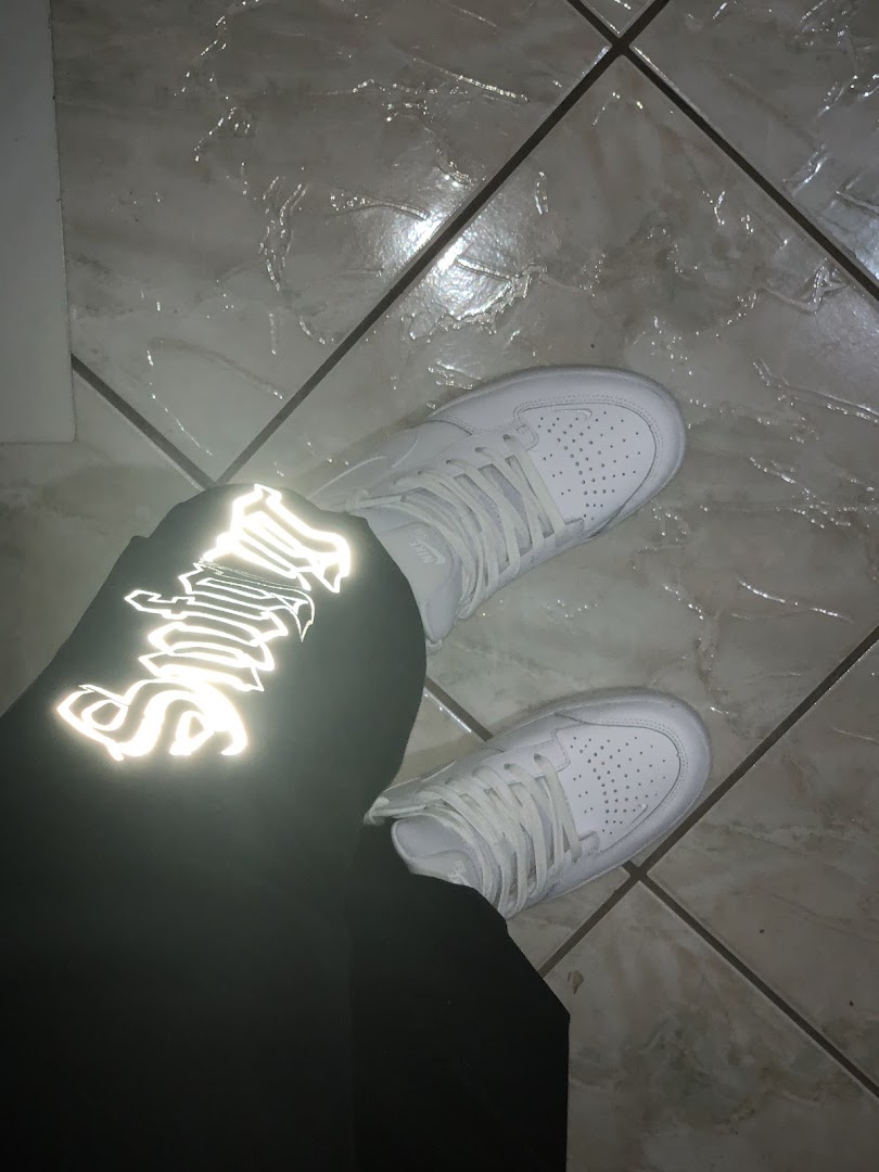A person wearing white sneakers and black pants with reflective lettering.