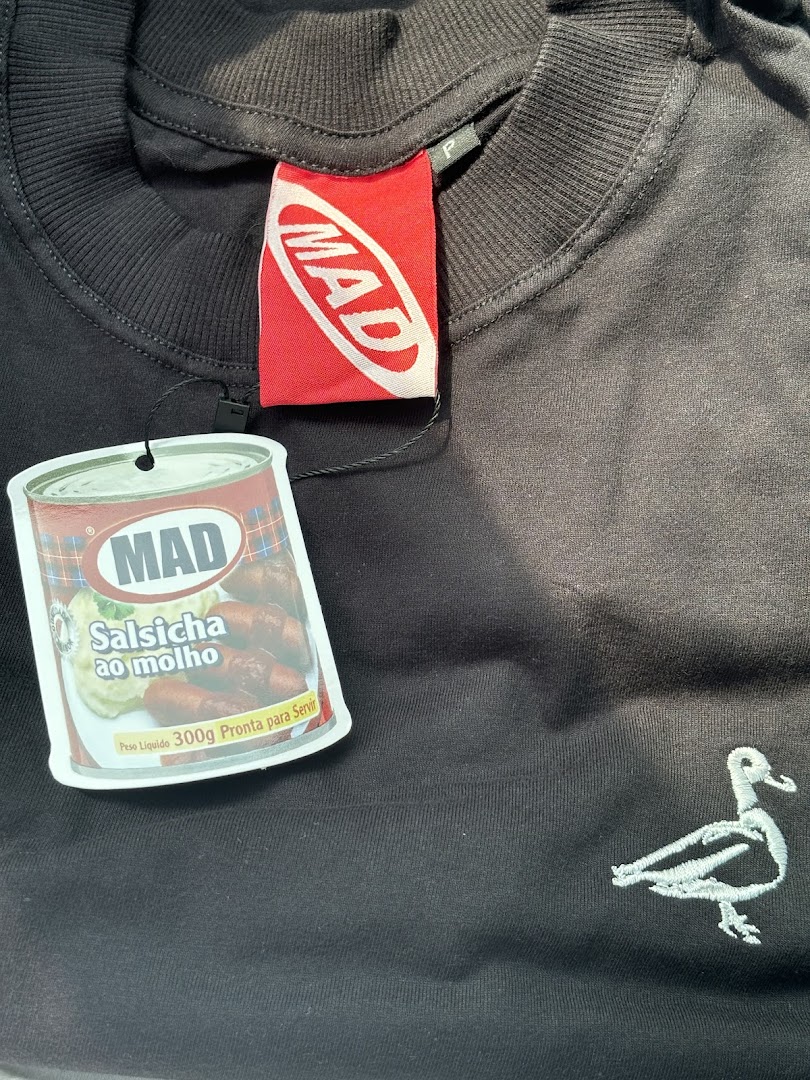 A black t-shirt with a red MAD brand tag and a novelty tag shaped like a can of sausages.