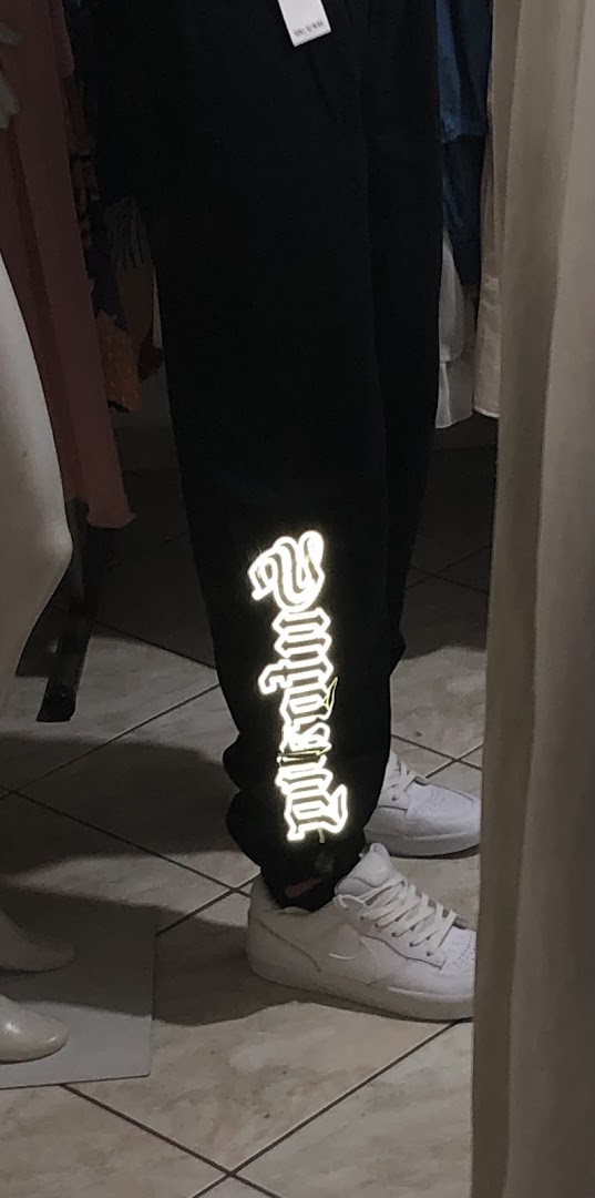 Close-up of black pants with reflective lettering and white sneakers.