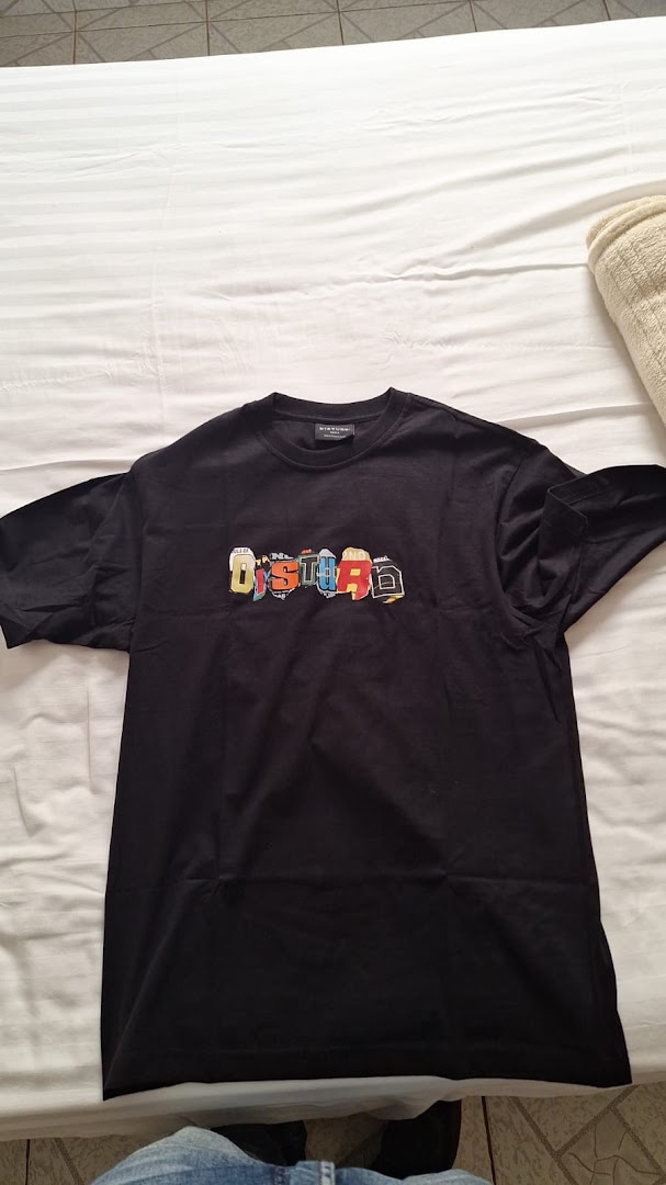 A black t-shirt with a colorful 'DISTURB' logo is laid out on a white surface.