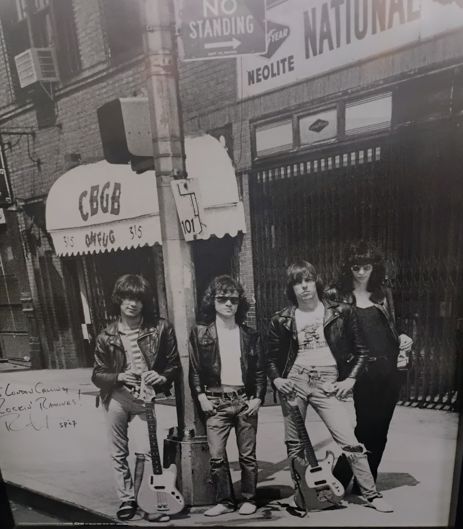 A black and white photo of four people dressed in punk rock attire with guitars outside a building.