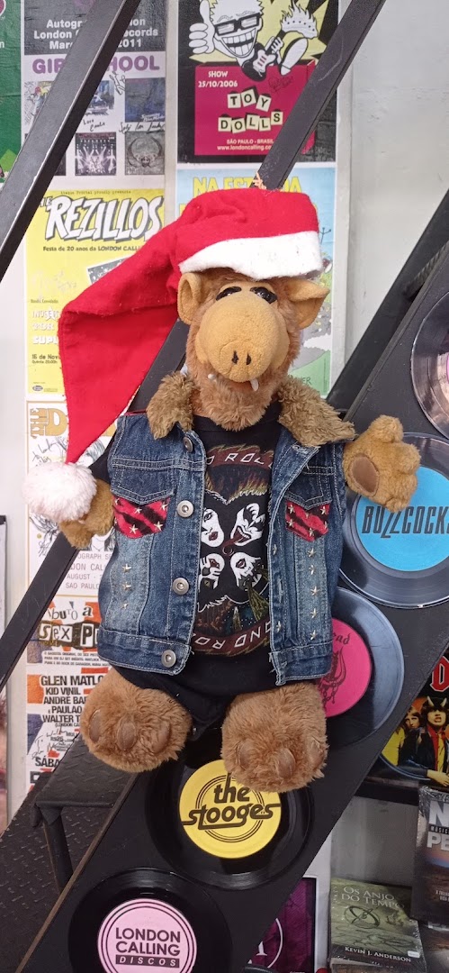 A plush toy dressed as a punk rocker with a Santa hat, surrounded by band posters and vinyl records.