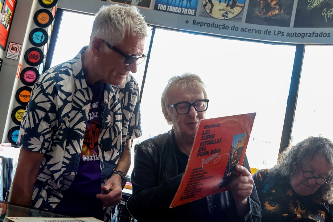 Three men are looking at a vinyl record in a shop filled with records.