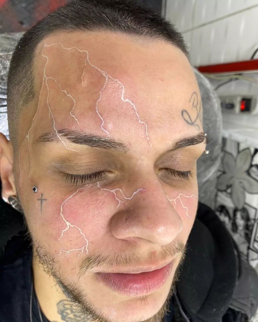 A close-up of a person's face with a white lightning bolt tattoo design.