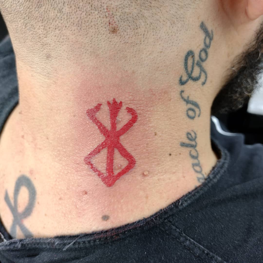 A close-up of a red tattoo on a person's neck, with other tattoos visible.