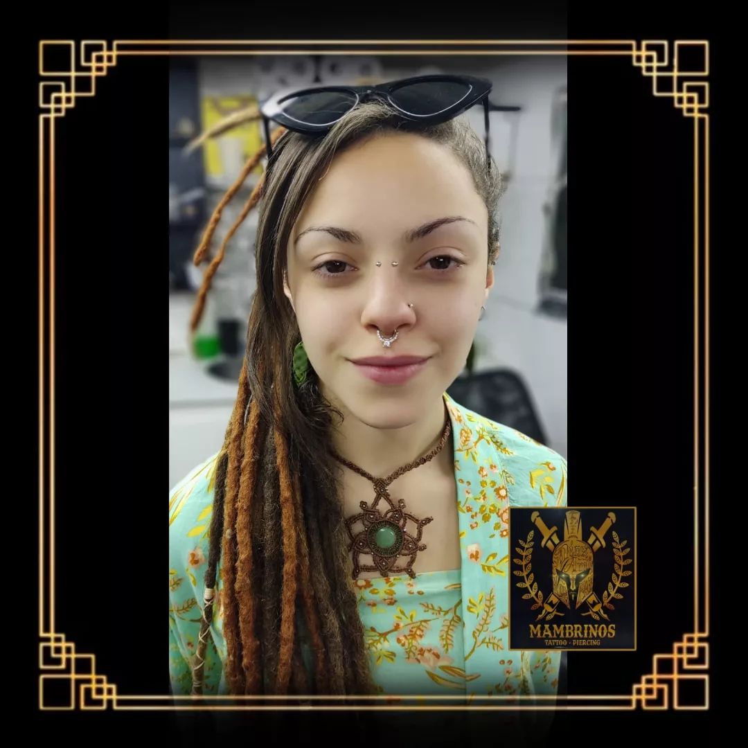 A young woman with dreadlocks and facial piercings smiles at the camera.