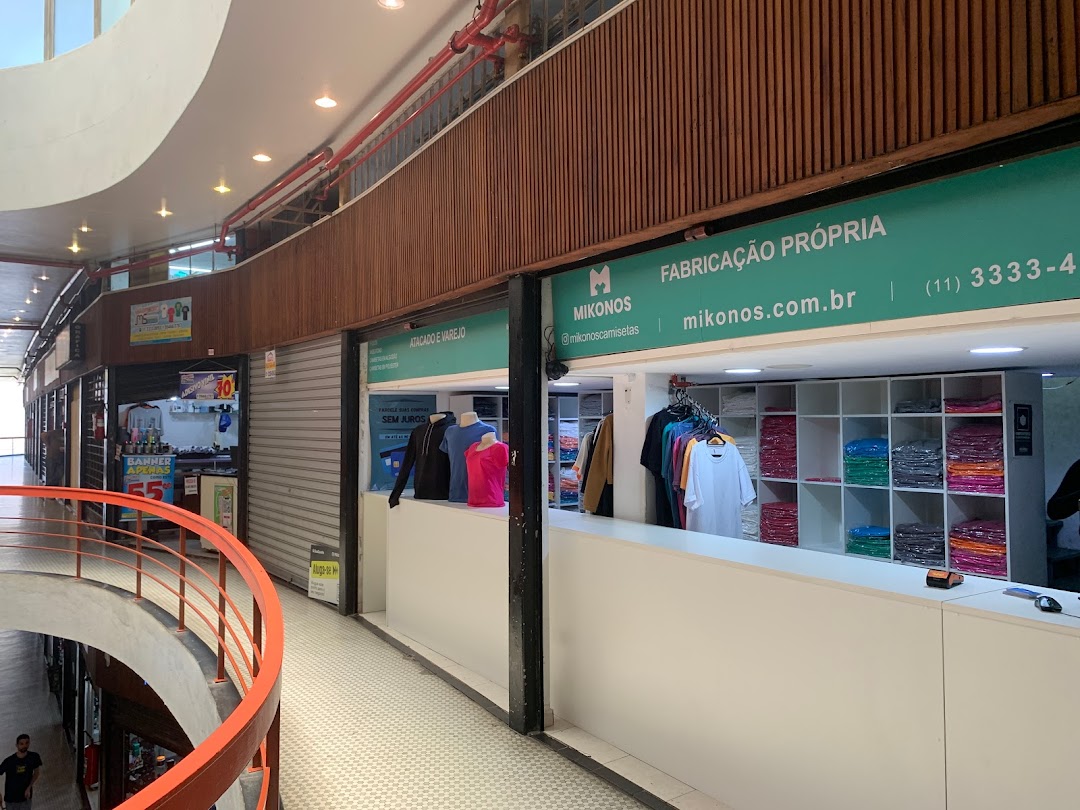 A clothing store called Mikonos with racks of t-shirts and a sign indicating 'Fabricação Própria'.