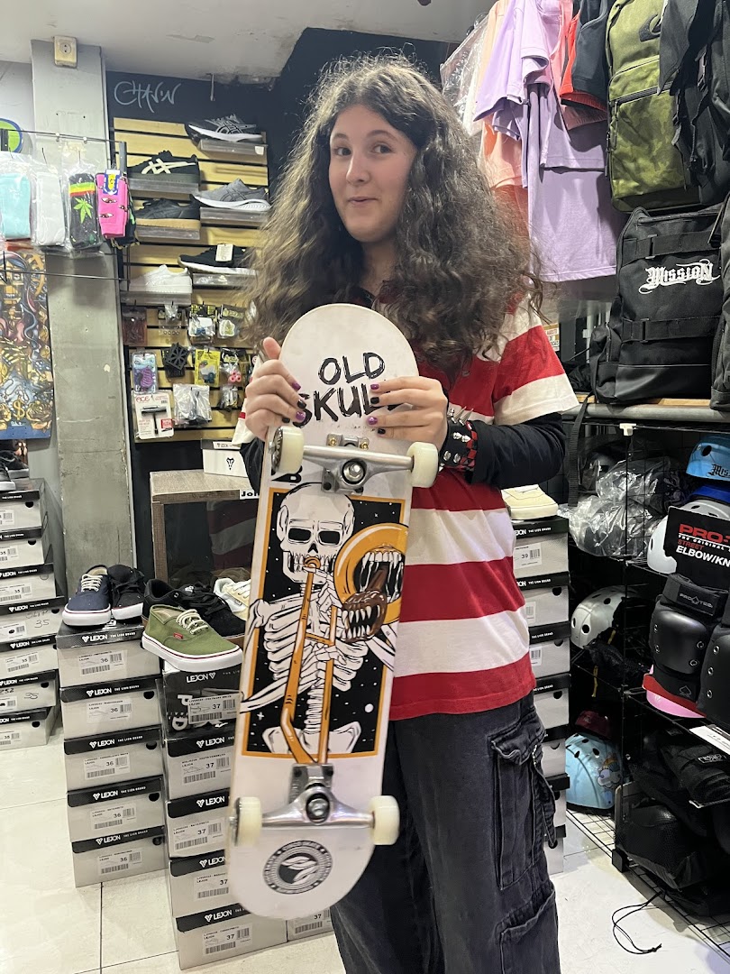 A person holds a skateboard with a skeleton graphic inside a skate shop.
