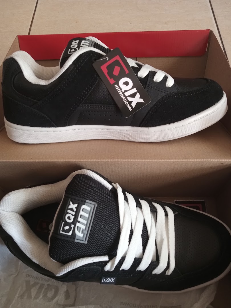 A pair of black QIX International skate shoes with white laces and soles, presented in a box.