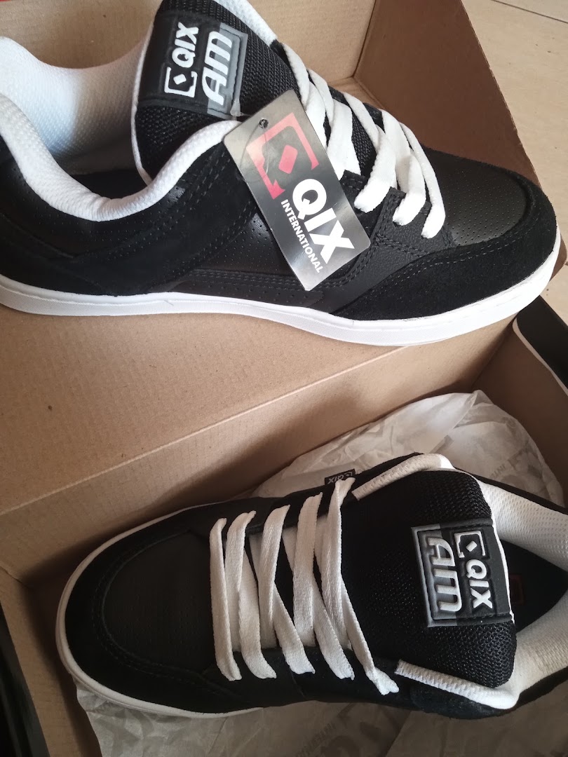 A pair of black and white QIX International skate shoes in a cardboard box.