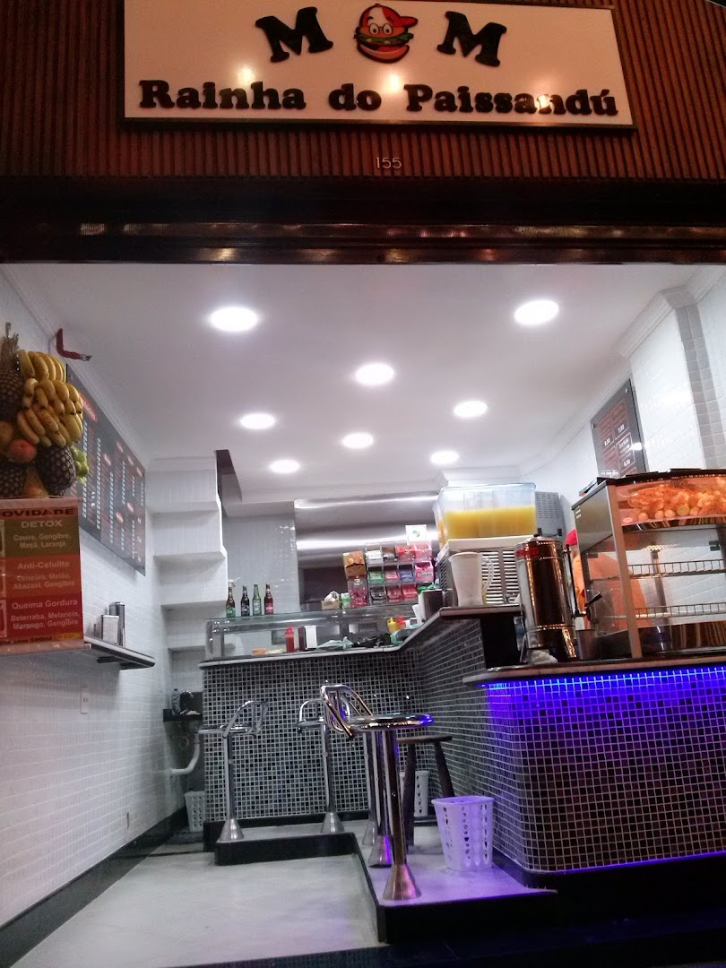The entrance of a food shop called MM Rainha do Paissandú, with a counter and seating.