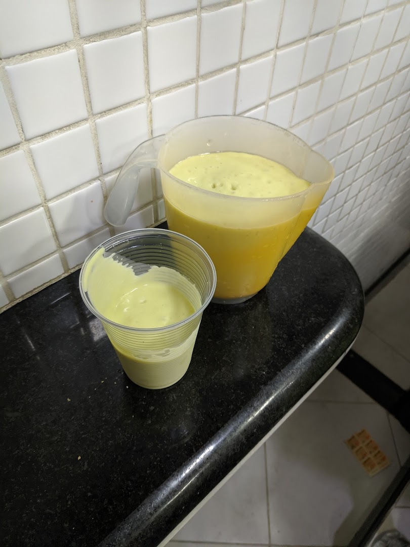 A plastic cup and a pitcher filled with a creamy yellow beverage.