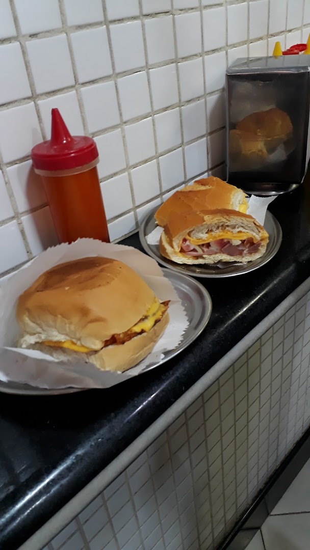 Two delicious sandwiches and a bottle of sauce on a counter with tiled walls.