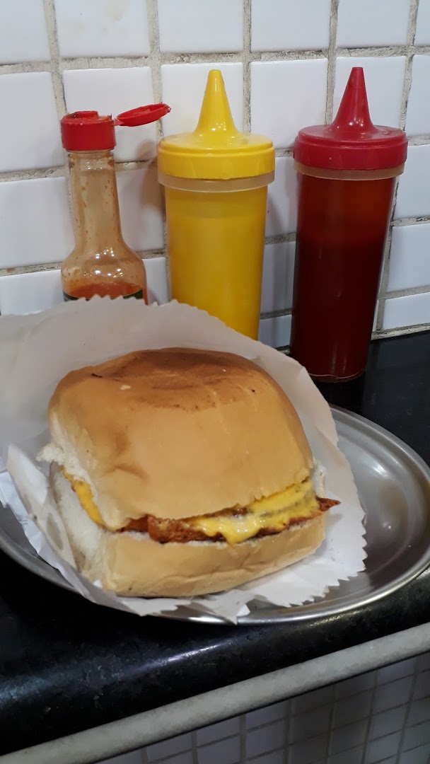 A delicious-looking burger with melted cheese, served with ketchup, mustard, and hot sauce bottles.
