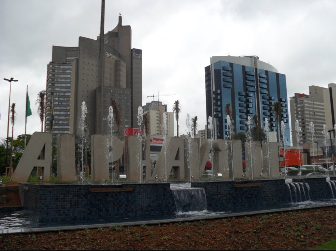Large concrete letters spelling 'ALPHA' with fountains in front of modern city buildings.