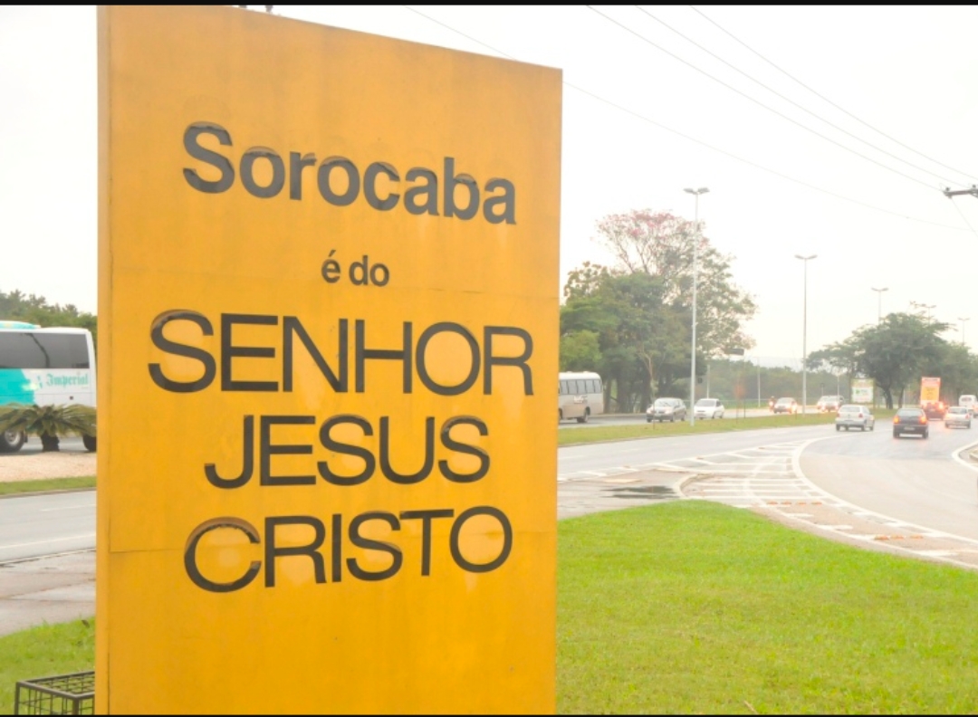 A large yellow sign with black text about faith is placed near a road with traffic.