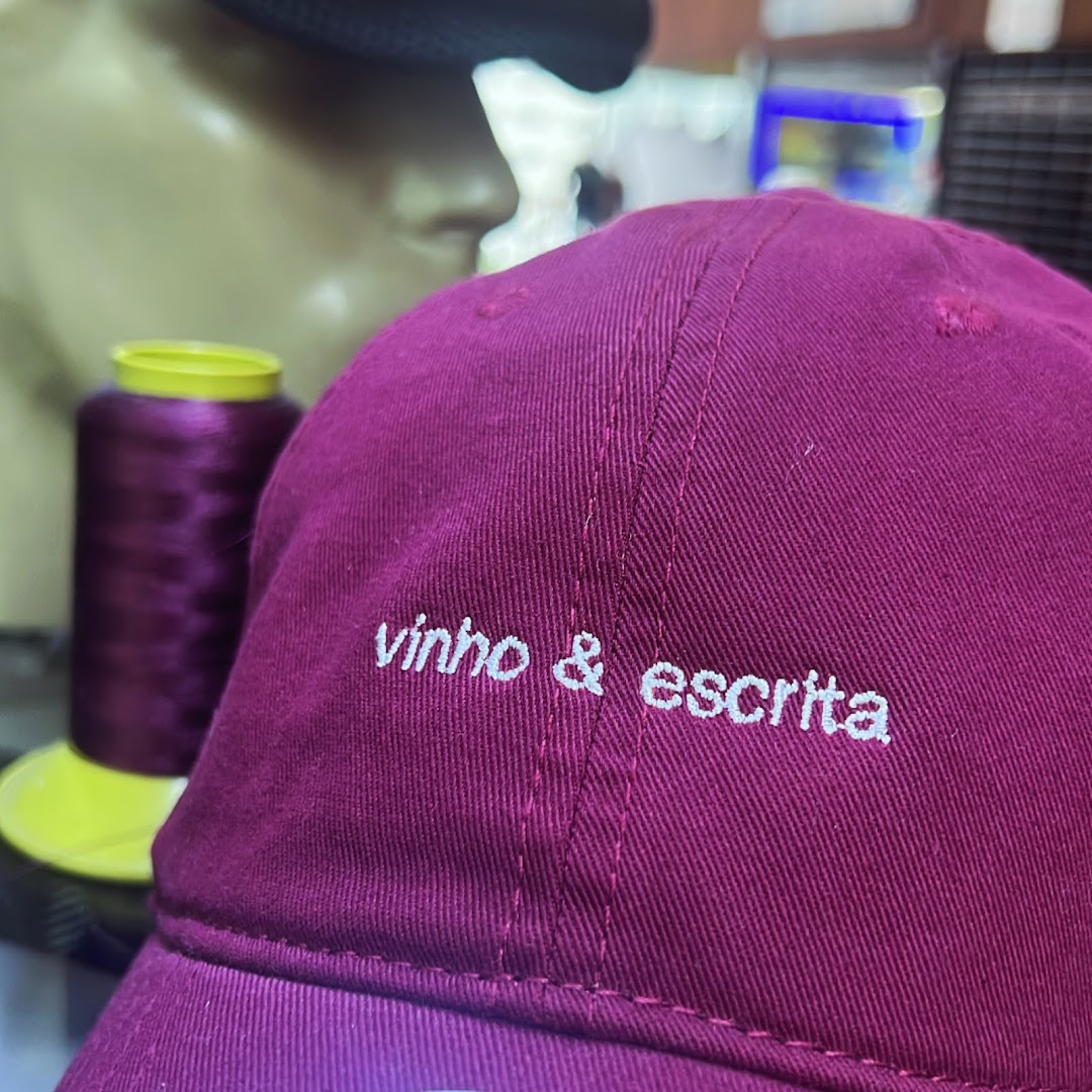 A close-up of a maroon cap with white embroidery and a spool of purple thread.