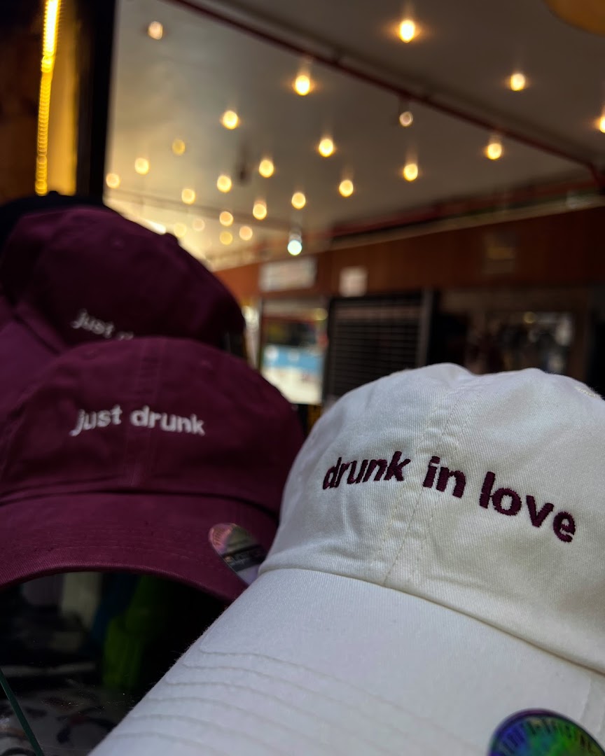 Close-up of two embroidered baseball caps, one white with 'drunk in love' and one maroon with 'just drunk'.