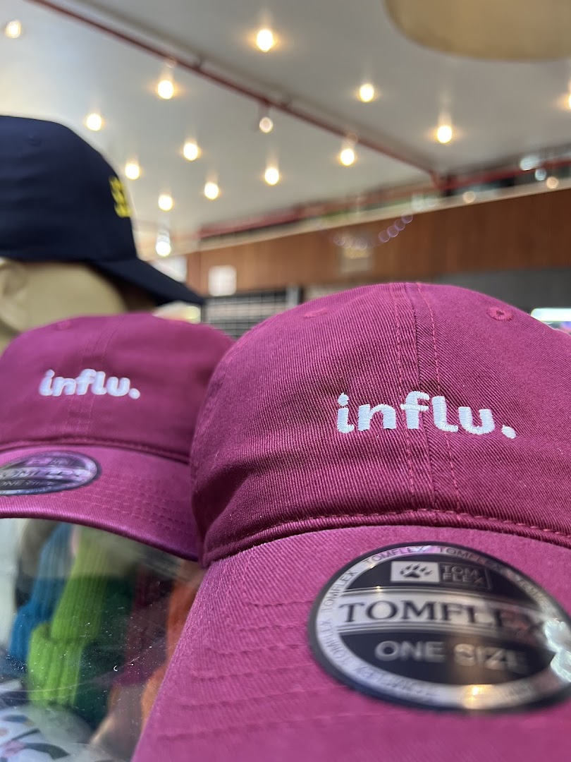 Close-up of burgundy baseball caps with 'influ.' embroidered on them.