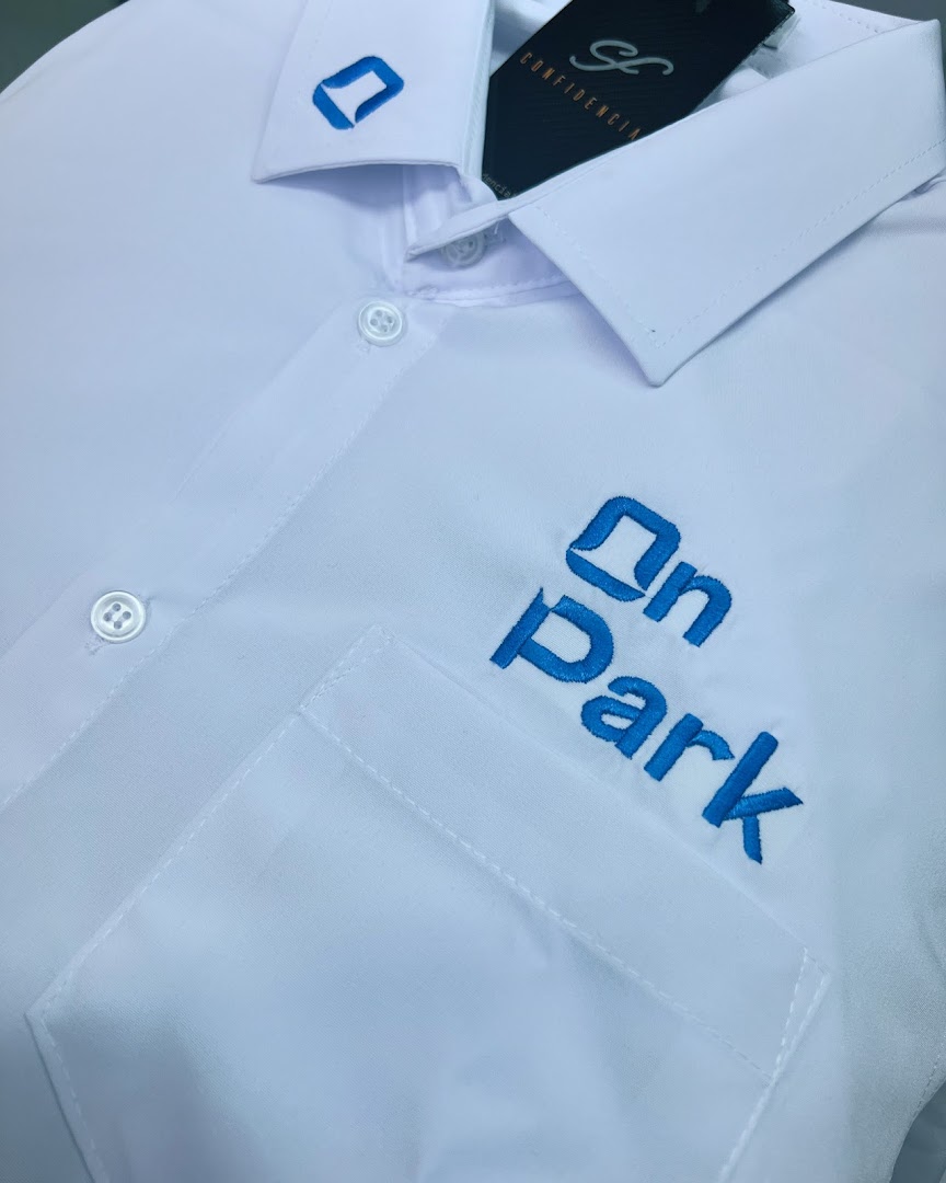 A close-up of a white collared shirt with blue embroidered text and logo.