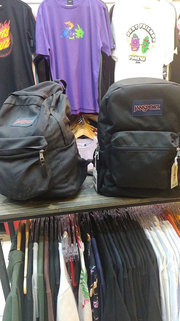 Two black Jansport backpacks displayed in front of a rack of graphic t-shirts.