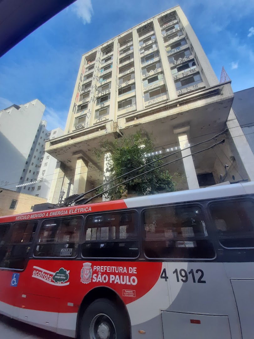 A bus with 'Preffeitura de São Paulo' branding passes by a building with graffiti.